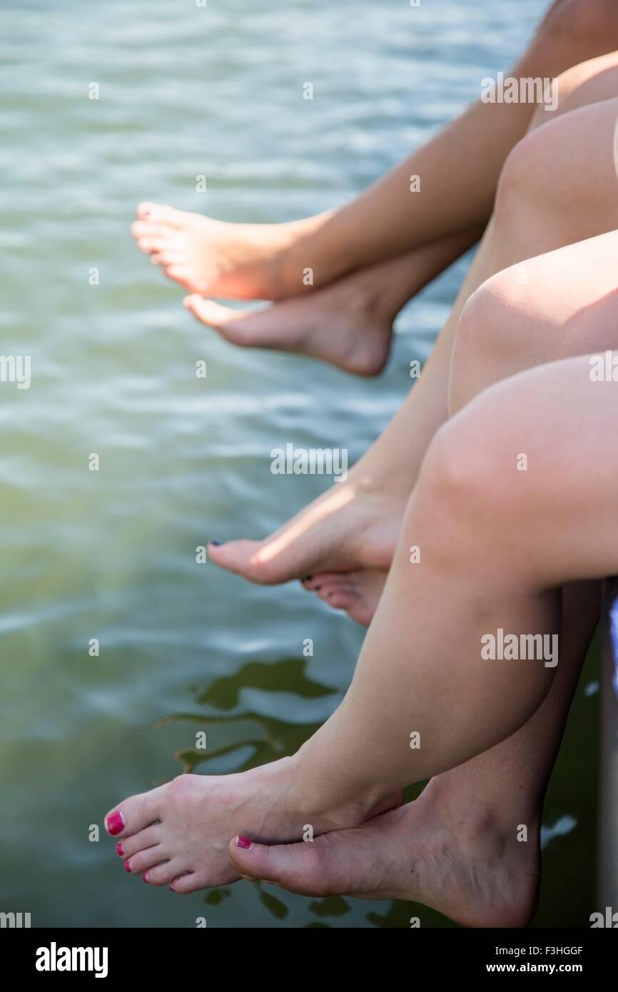 Gambe di tre giovani donne penzolante dal lago di pier Foto Stock