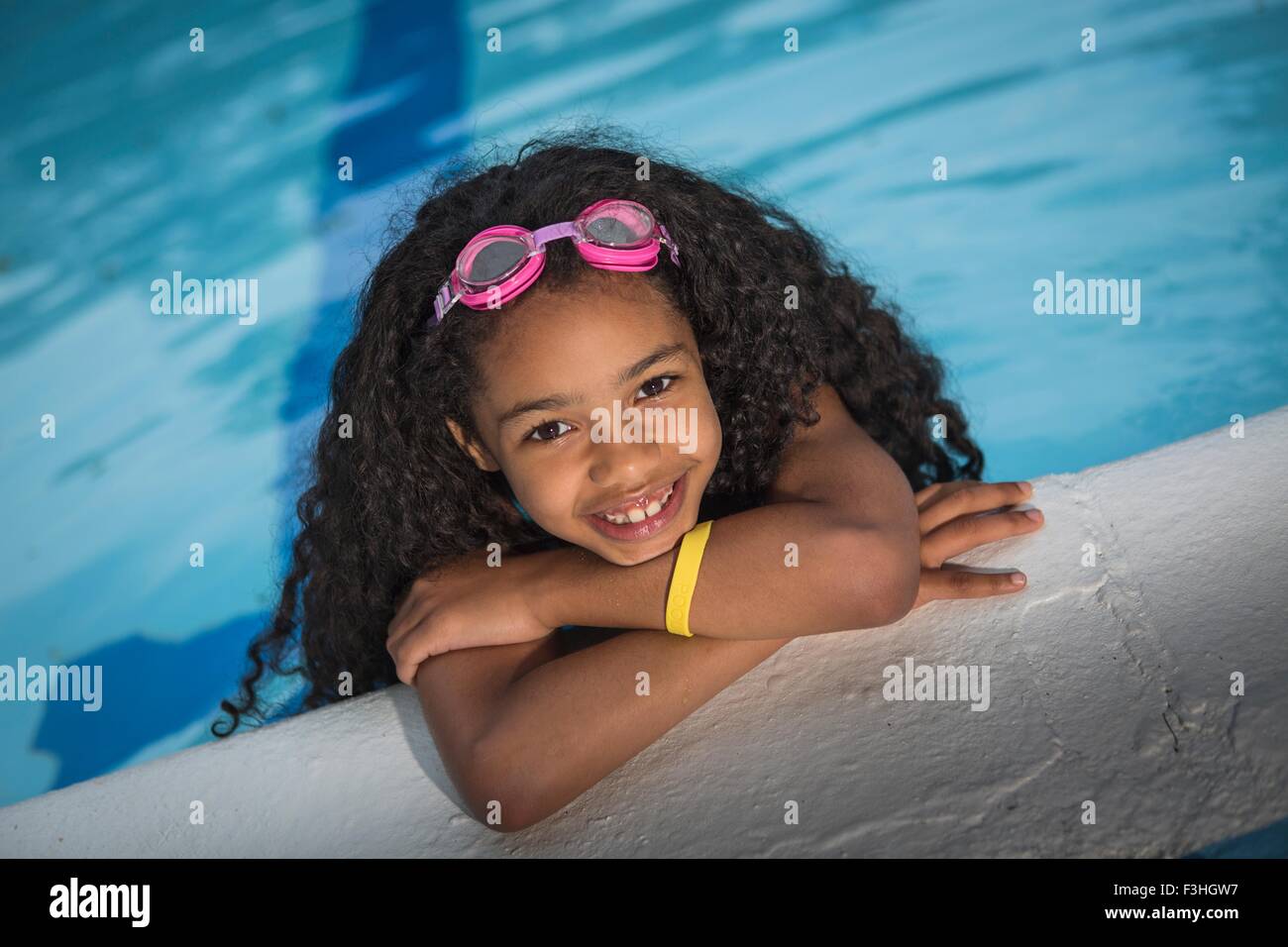 Ritratto di ragazza con ricci capelli neri appeso sul bordo della piscina, guardando alla fotocamera a sorridere Foto Stock
