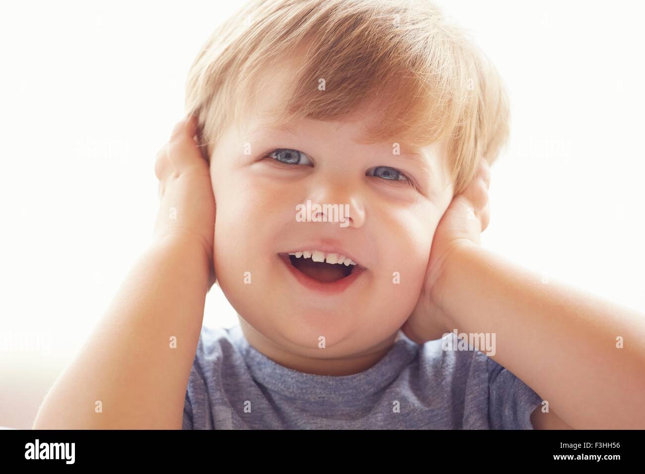 Ritratto di giovane ragazzo che copre le orecchie con le mani, guardando lontano sorridente Foto Stock