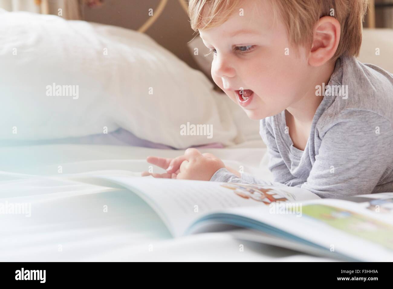 La testa e le spalle del ragazzo disteso sul letto sulla parte anteriore, in appoggio sui gomiti guardando storybook Foto Stock