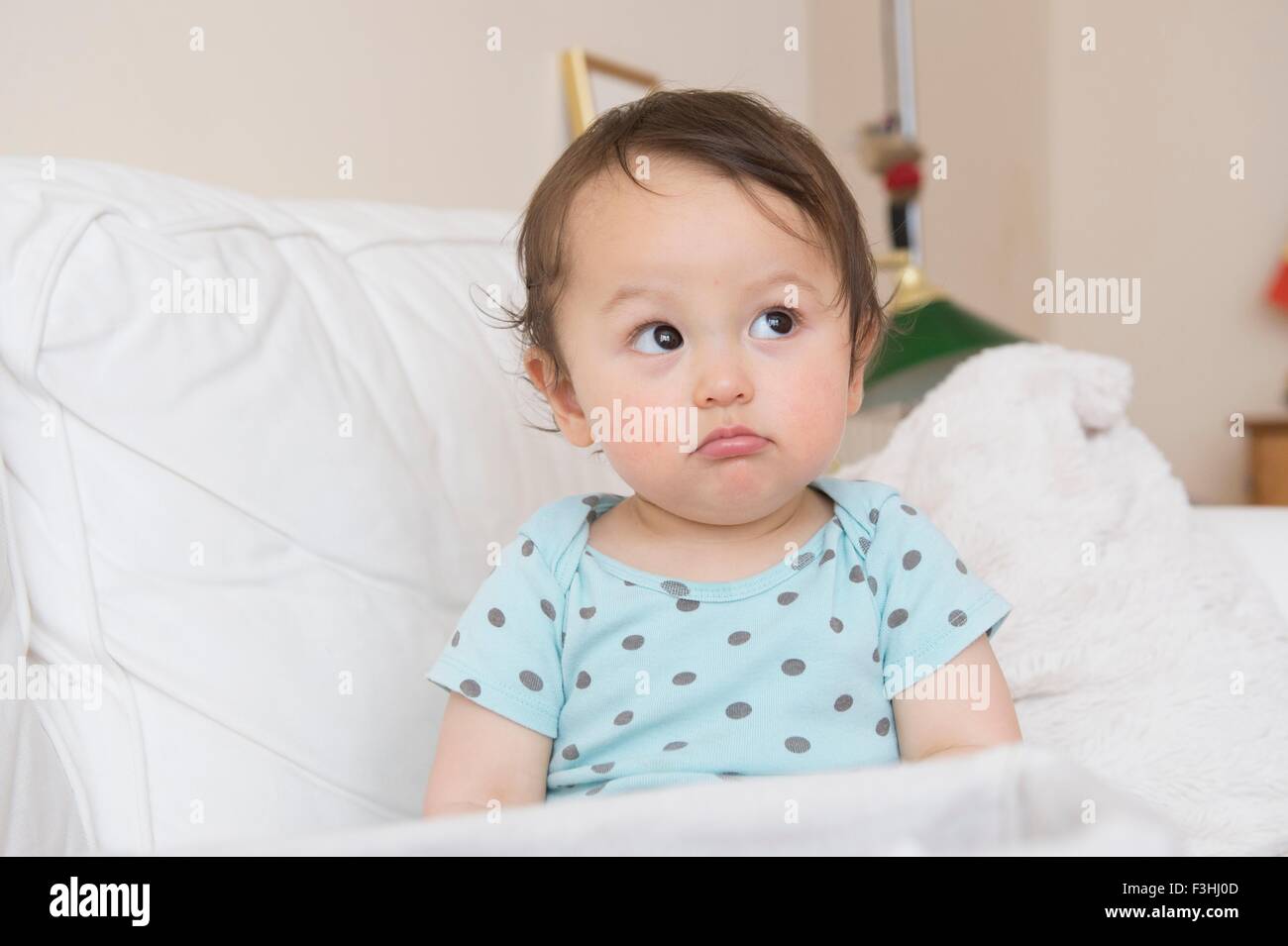 Bambino seduto sul divano tirando la faccia e guardando lateralmente Foto Stock