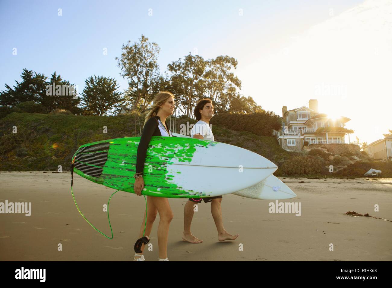 Giovane camminando verso il mare, portando le tavole da surf Foto Stock