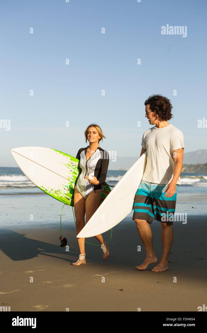 Giovane camminando sulla spiaggia, portando le tavole da surf Foto Stock