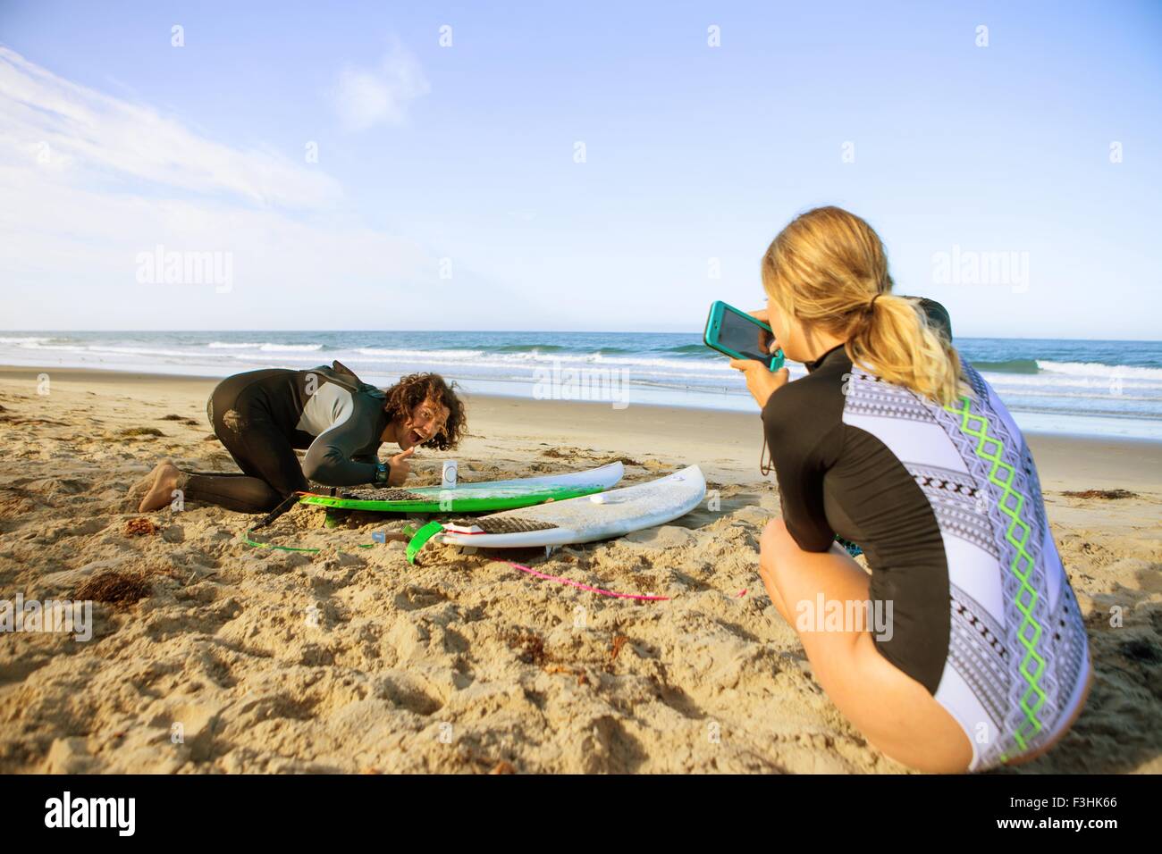 Coppia sulla spiaggia, giovane donna prendendo fotografia di uomo con la tavola da surf Foto Stock