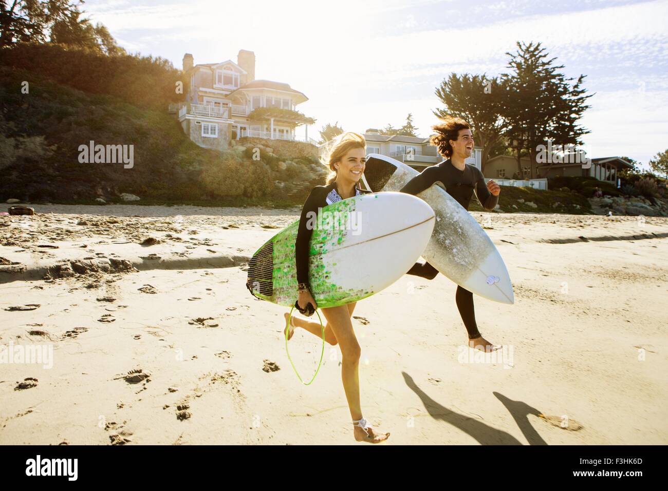 Giovane che corre verso il mare, portando le tavole da surf Foto Stock