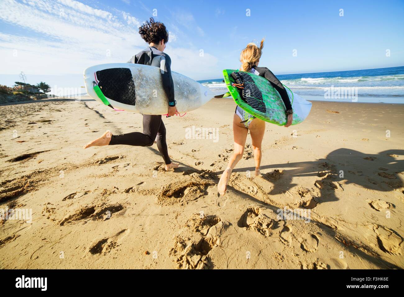 Giovane che corre verso il mare, portando le tavole da surf, vista posteriore Foto Stock
