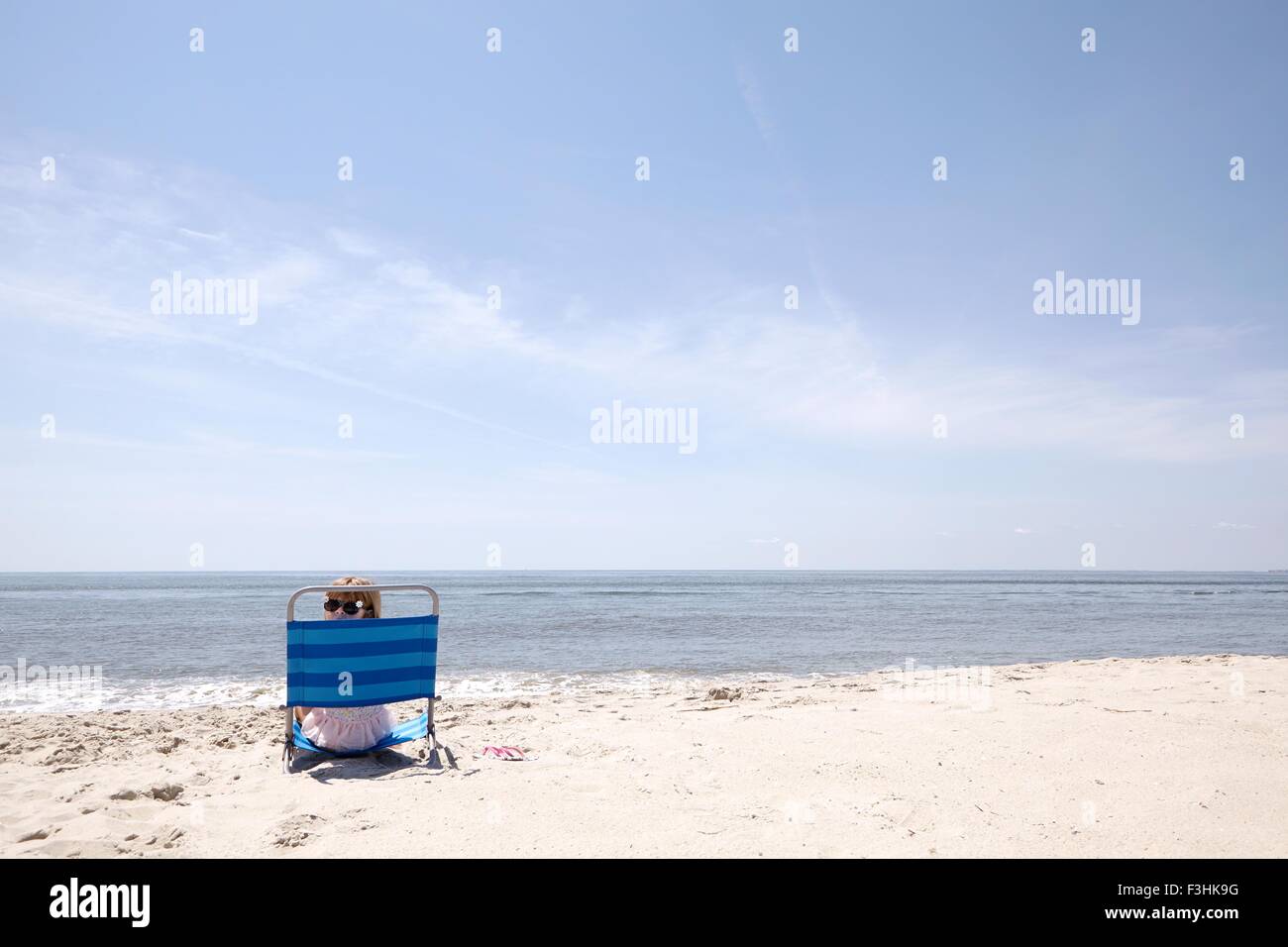 Ragazza guardando sopra la sua spalla dalla sedia a sdraio sulla spiaggia Foto Stock