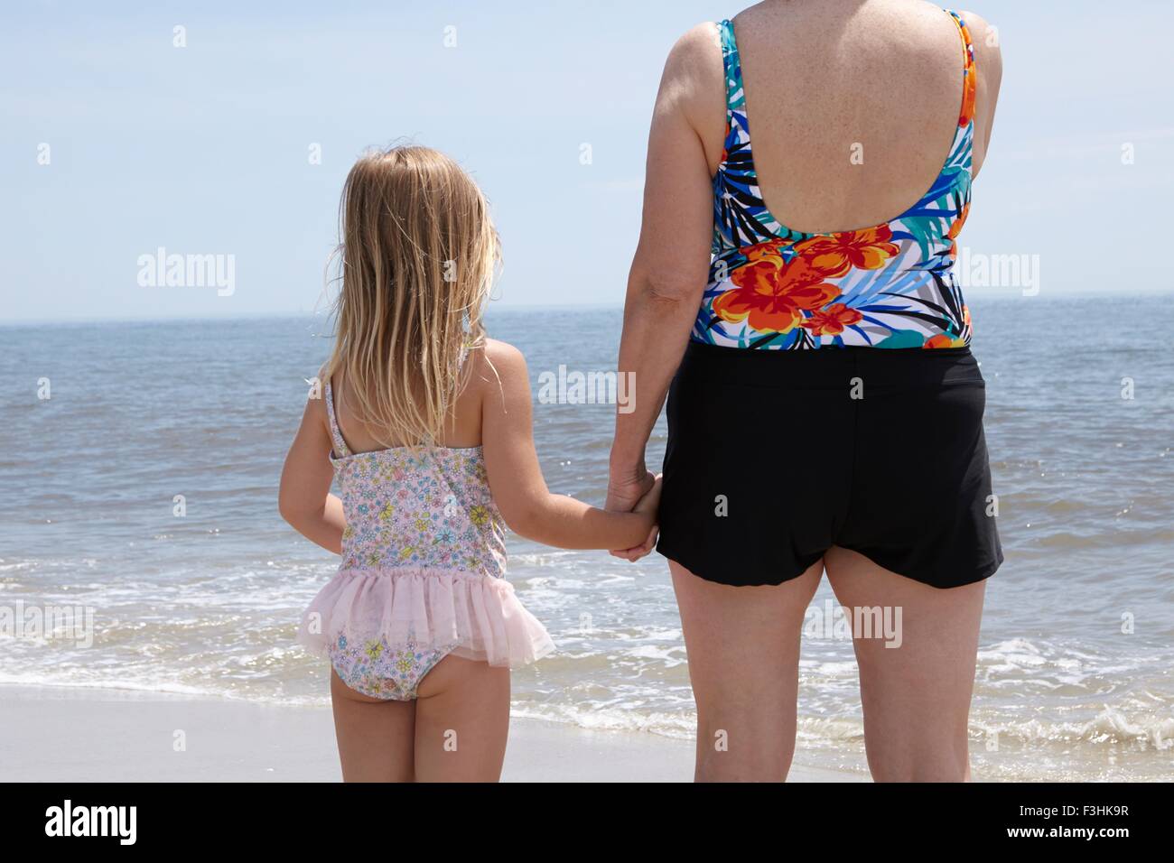Vista posteriore della donna senior e nipote tenendo le mani sulla spiaggia Foto Stock