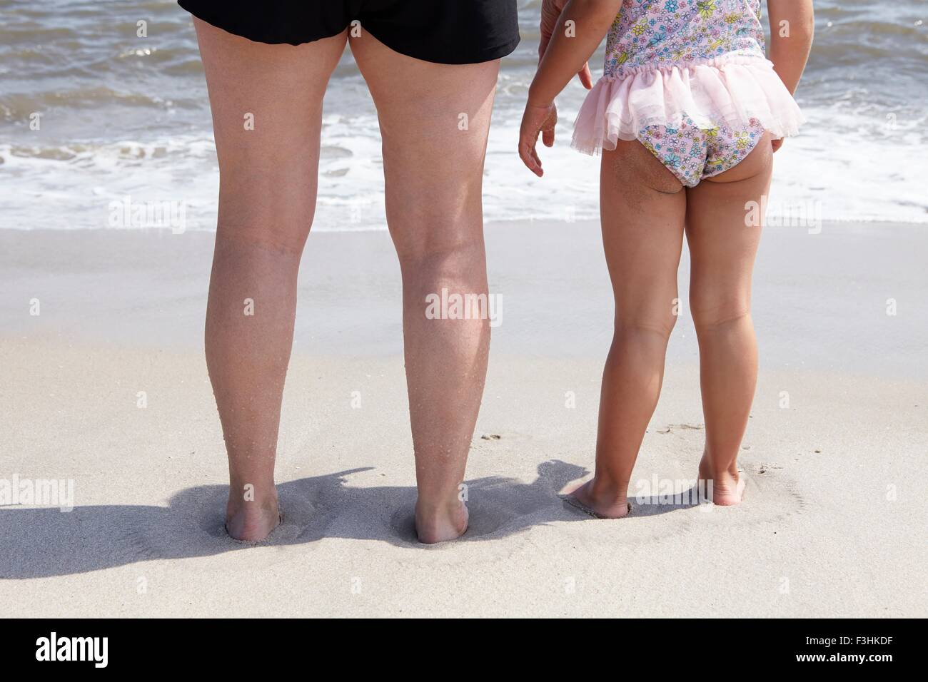 Posteriore vista ritagliata della donna senior e nipoti gambe sulla spiaggia Foto Stock