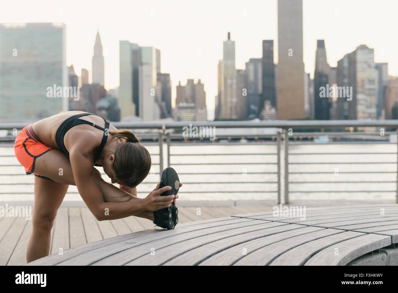 Giovane donna in abiti in esecuzione accanto al fiume stretching prima di esercizio Foto Stock