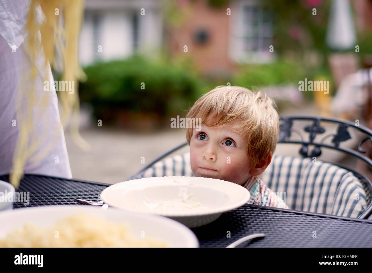 Ragazzo seduto al tavolo da giardino in attesa di spaghetti per essere servito Foto Stock