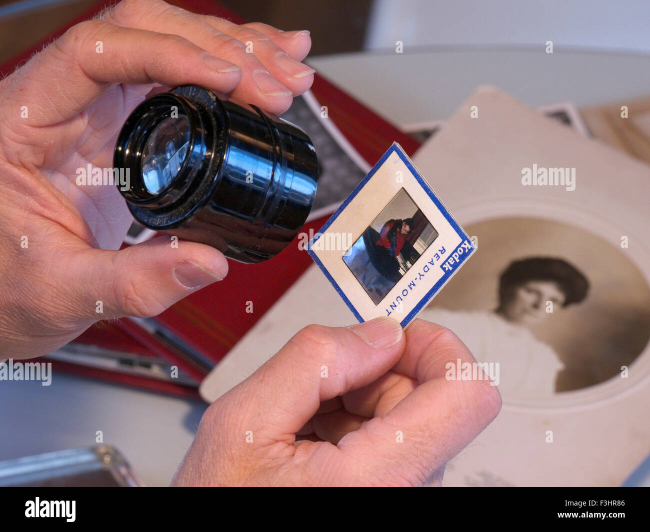 L uomo lo smistamento attraverso la storica famiglia ephemera, documenti, album fotografici e i lucidi a colori con occhio lupe di vetro Foto Stock