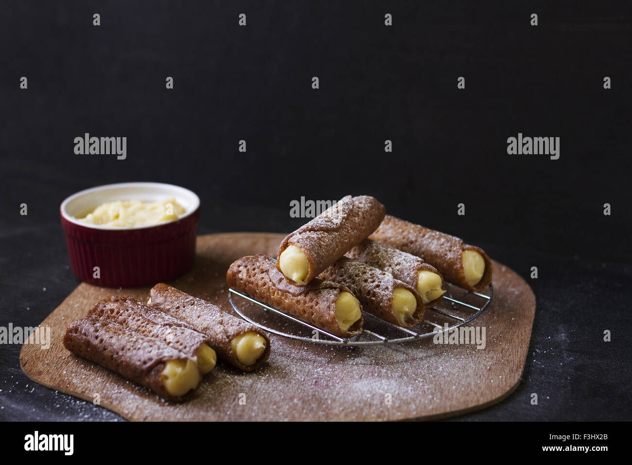 Brandysnaps con panna fresca e zucchero a velo su legno scheda servente Foto Stock