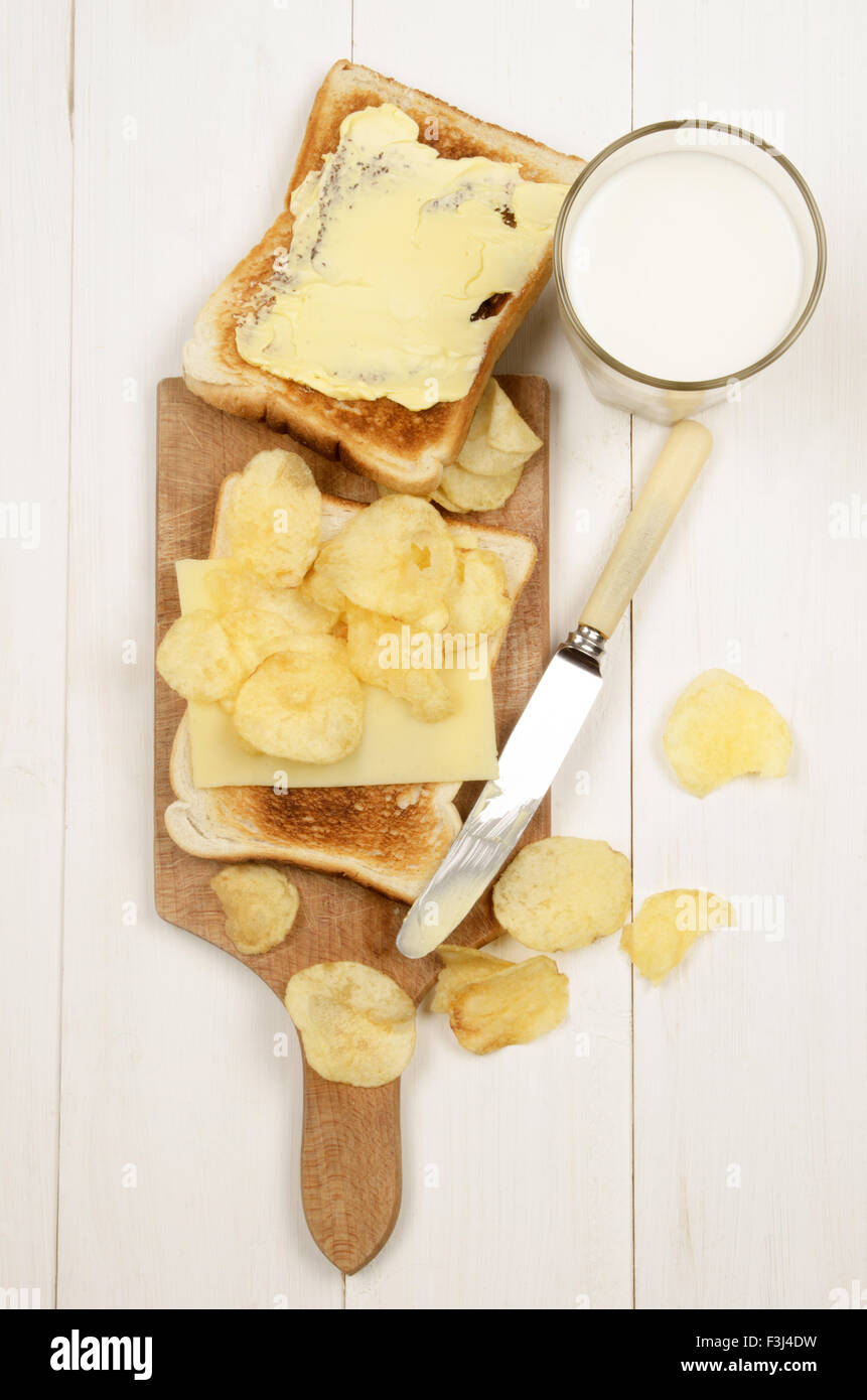 Pane tostato con una fetta di dolce cheddar irlandese, patatine salate e un bicchiere di latte fresco Foto Stock