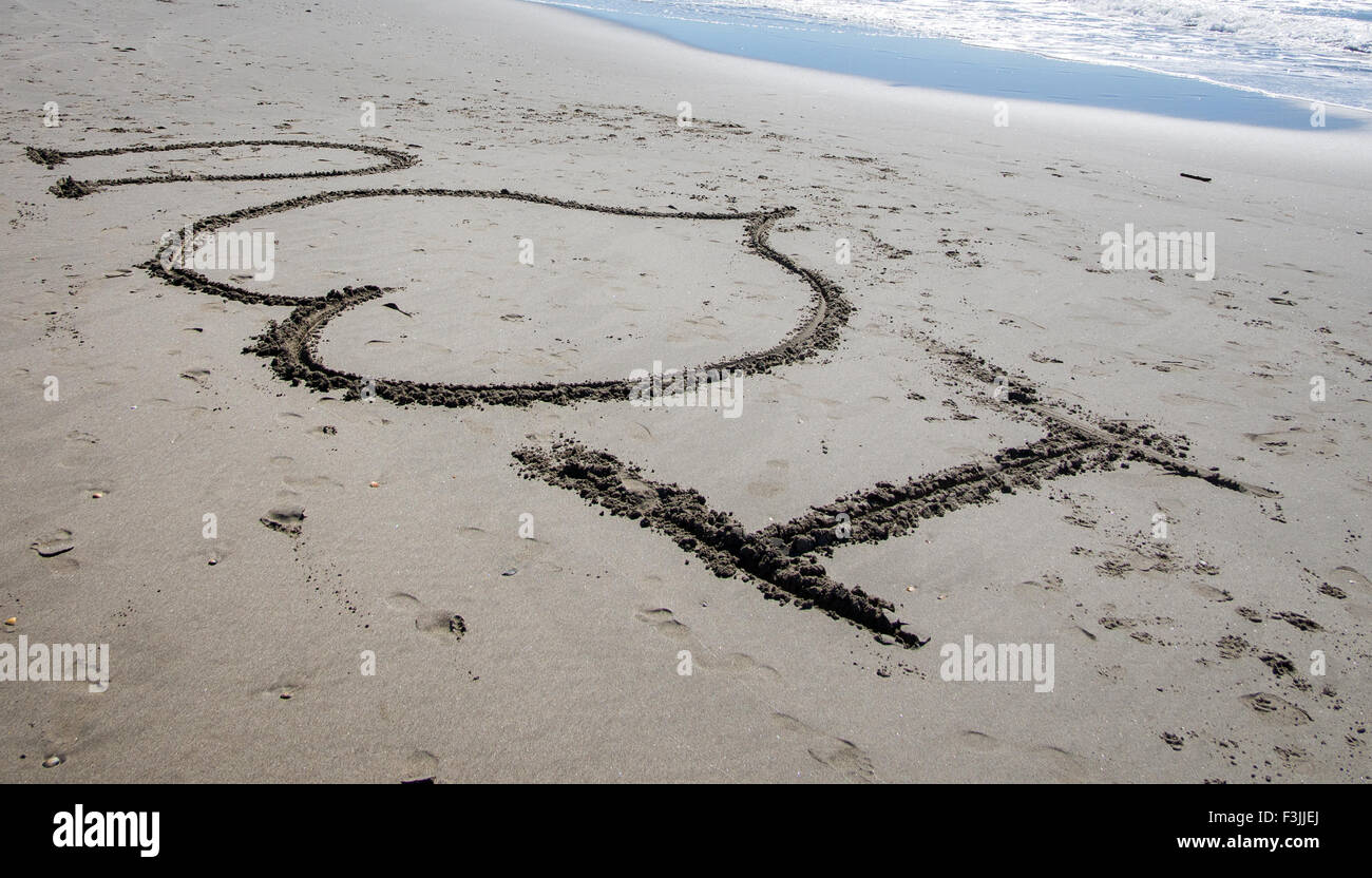 I "cuore" u scritto di sabbia su una spiaggia in Francia. Un'onda si rompe nell'angolo in alto a destra. Il cuore simboleggia l'amore. Foto Stock