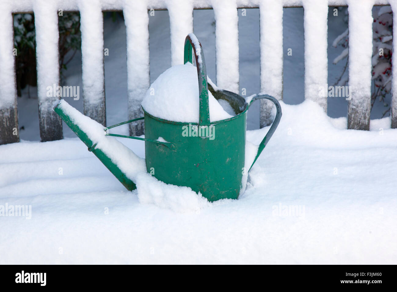 Stagioni fine un giardino annaffiatoio sinistra sul sedile del giardino nella neve Foto Stock