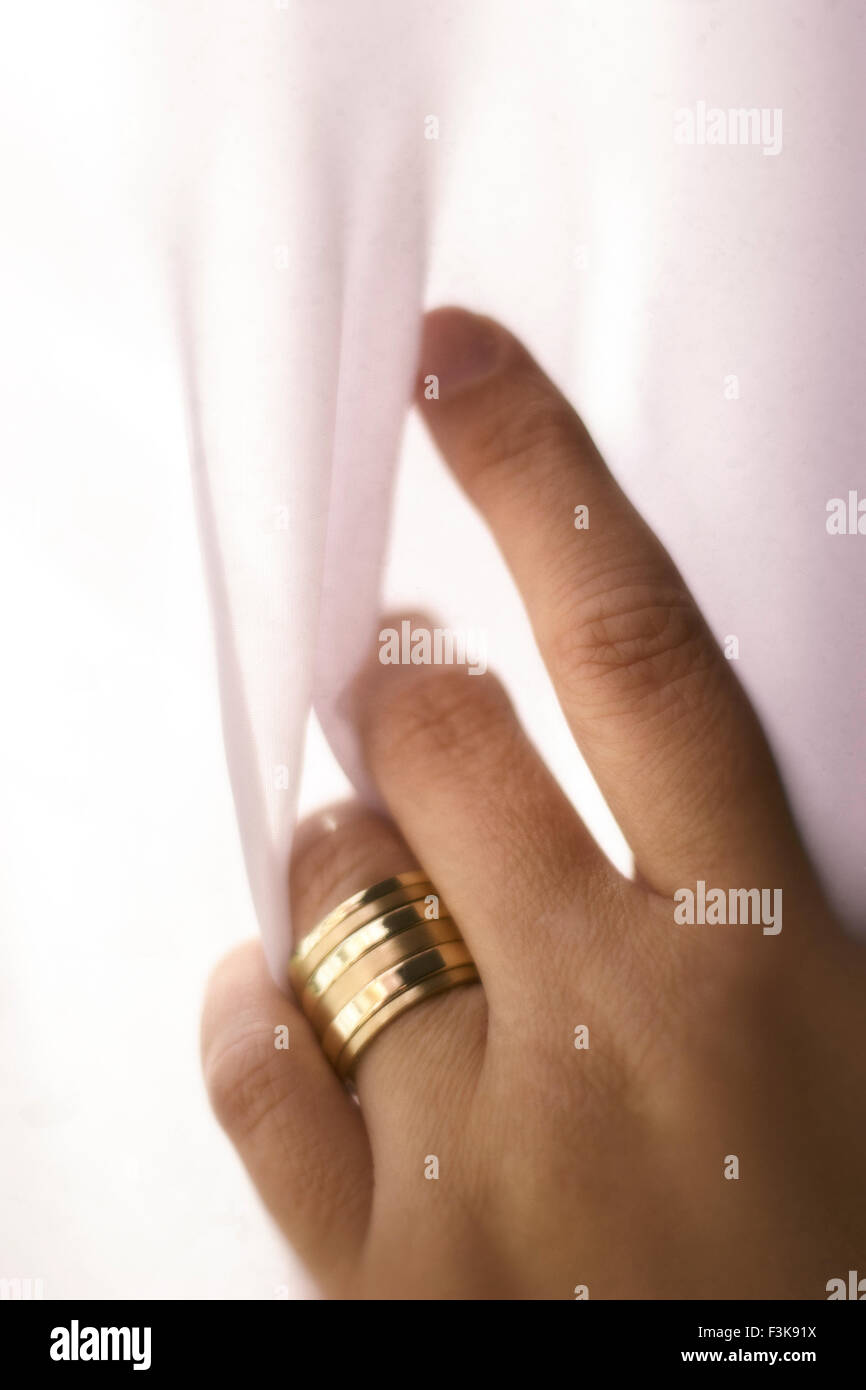 Una femmina di mano con bande in oro/anelli di nozze di tenere su una cortina di pura e semplice. Foto Stock