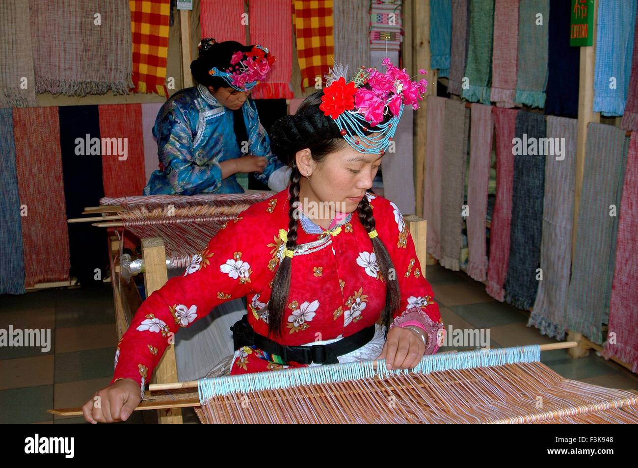 Lijiang, Cina: Naxi donne vestiti in abiti tradizionali lavorando su telai in un negozio di tessuti su Qi Yi Street Foto Stock