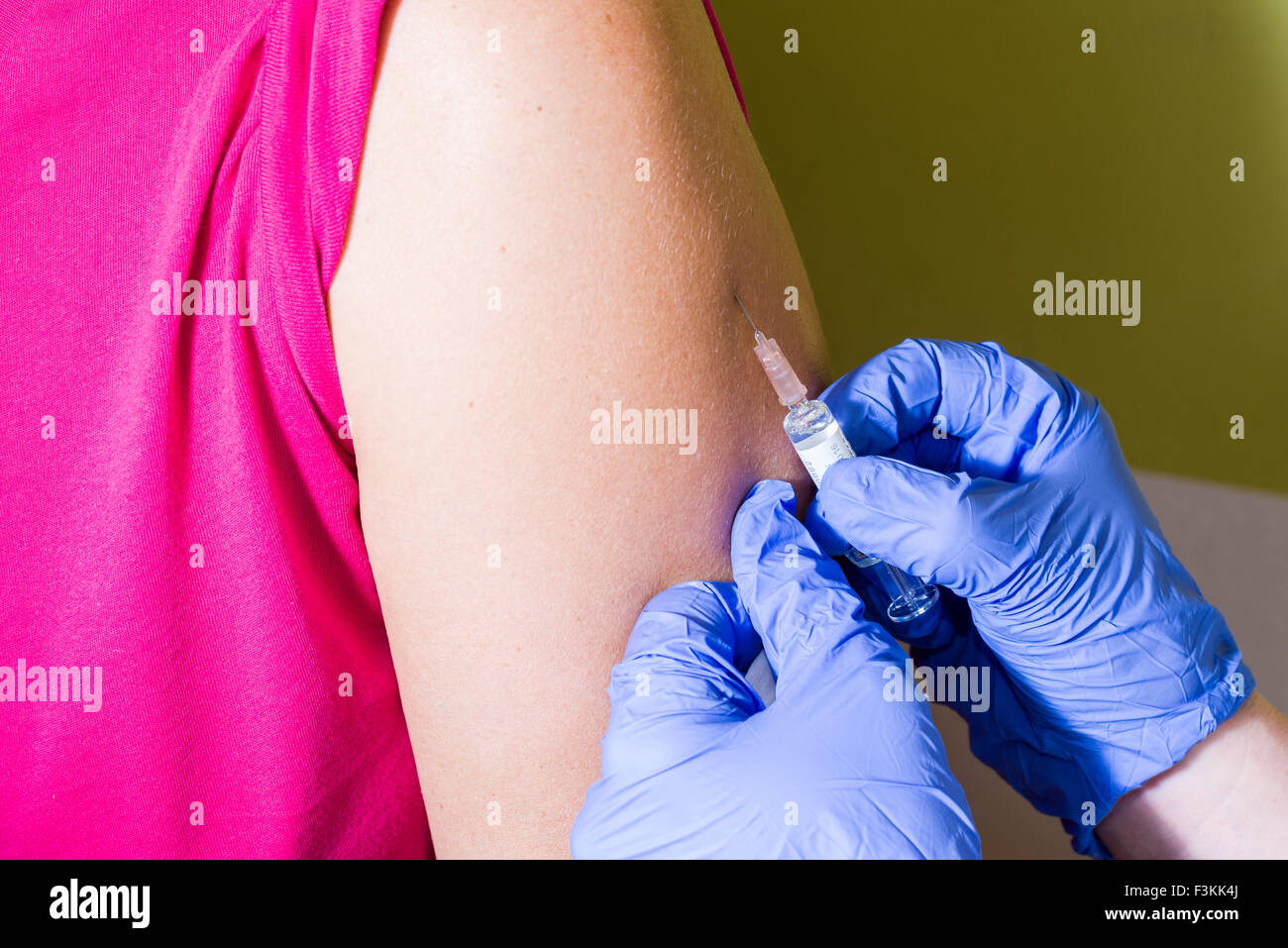 Una iniezione di medicina di fluido in un braccio di pazienti è fatto da due mani indossando guanti blu Foto Stock