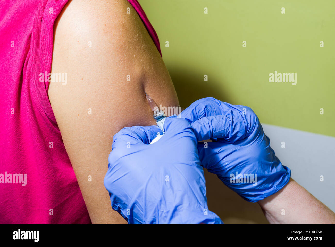 Una iniezione di medicina di fluido in un braccio di pazienti è fatto da due mani indossando guanti blu Foto Stock