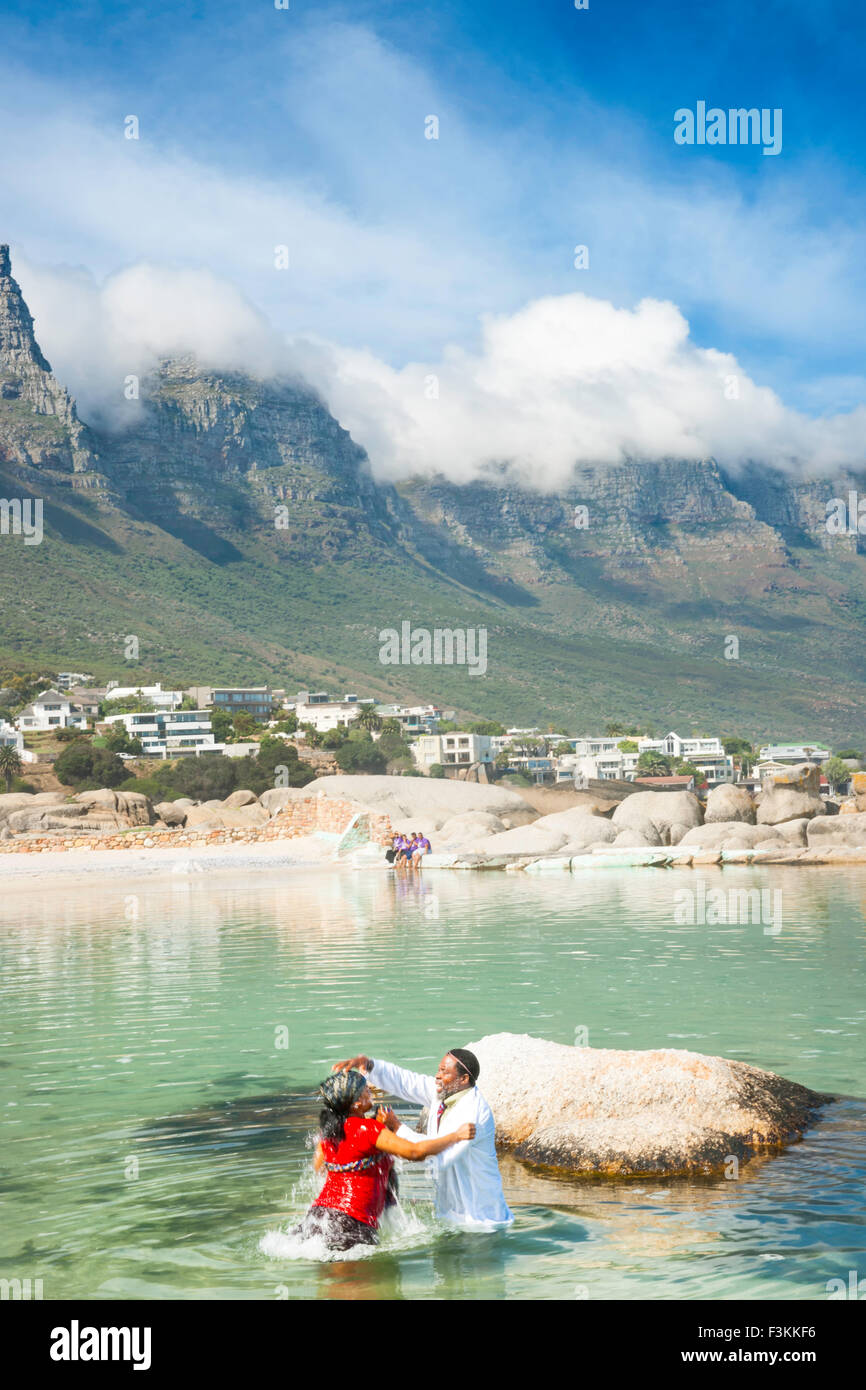 Sangoma guaritore battezza una donna nell'Oceano Atlantico, Table Mountain dodici Apostoli in background, Camp's Bay, Città del Capo, in modo Foto Stock