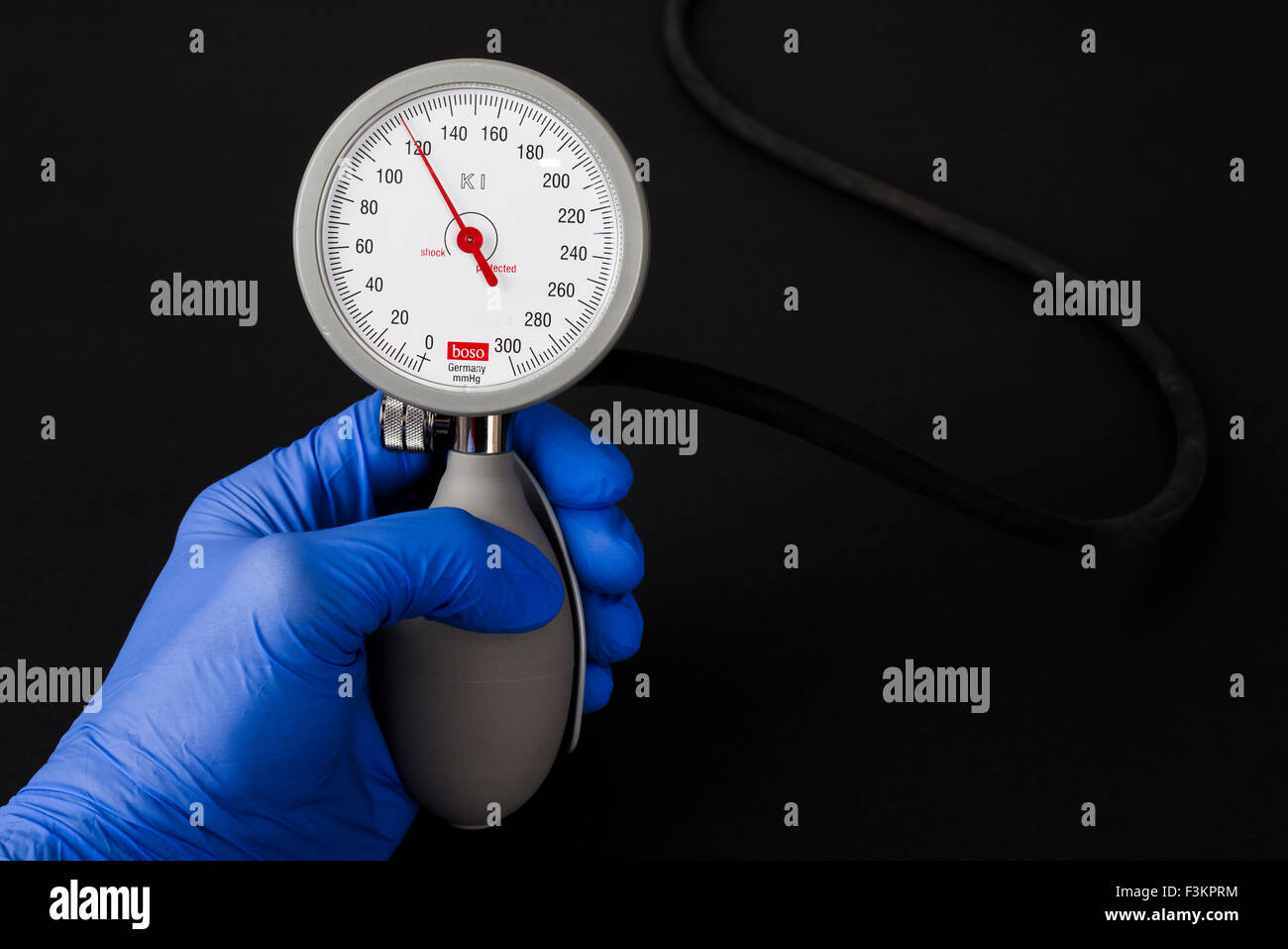 Una mano in una blu guanto medicale è in possesso di un sphygomanometer, sangue misuratore di pressione per uso medico, per indicare il normale sangue pres Foto Stock