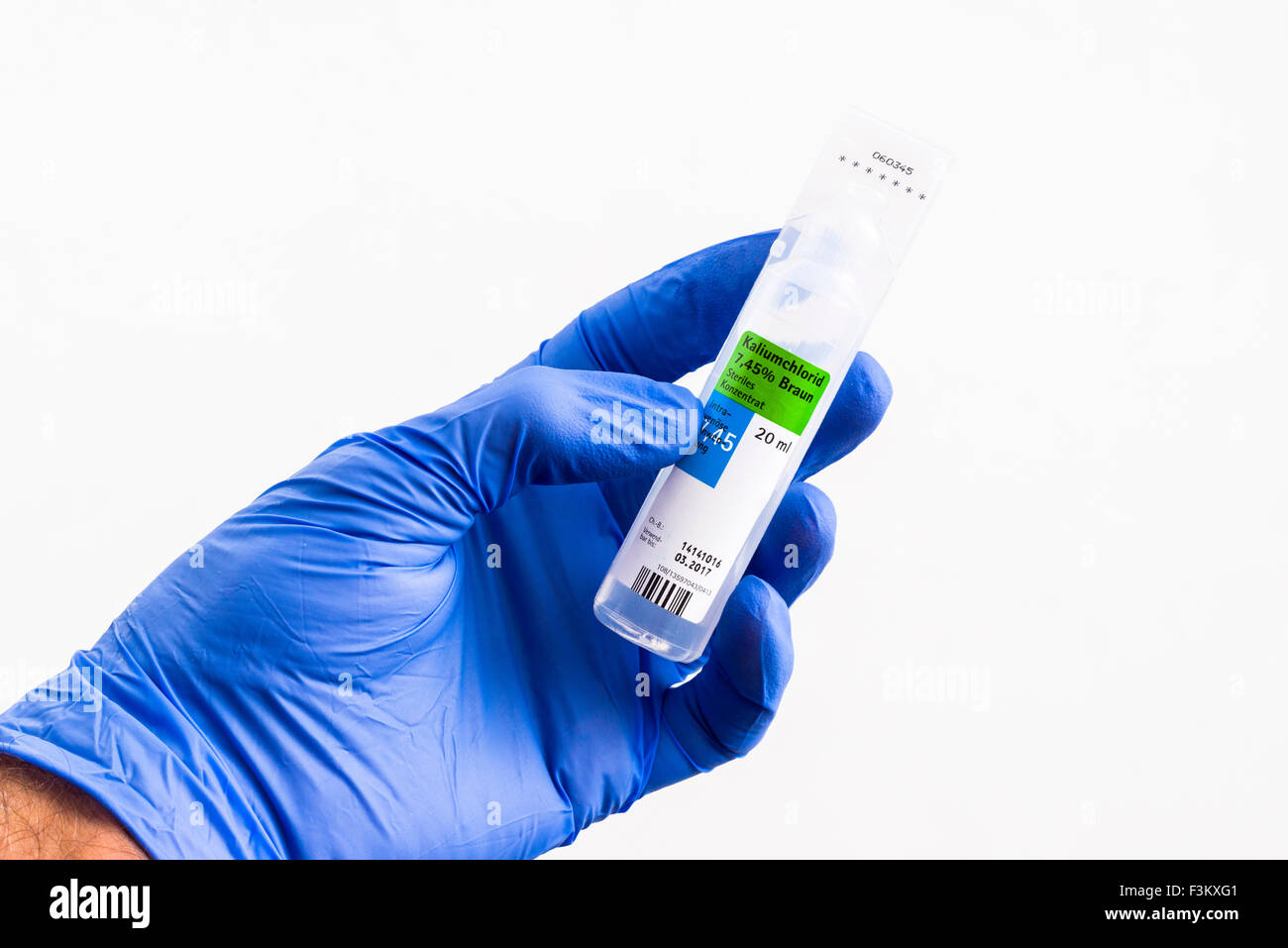 Una mano in una blu guanto medicale è in possesso di una bottiglia di plastica contenente cloruro calium per uso medico, visualizzato su un tavolo bianco Foto Stock