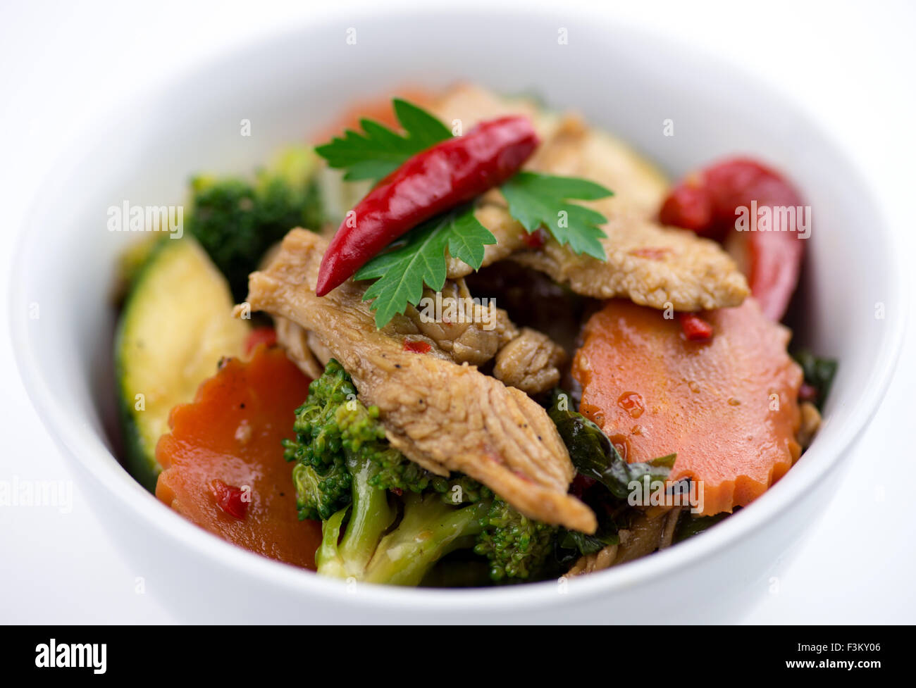 Di pollo tailandese con basilico carote, zucchine, peperoni e broccoli in una ciotola bianco Foto Stock