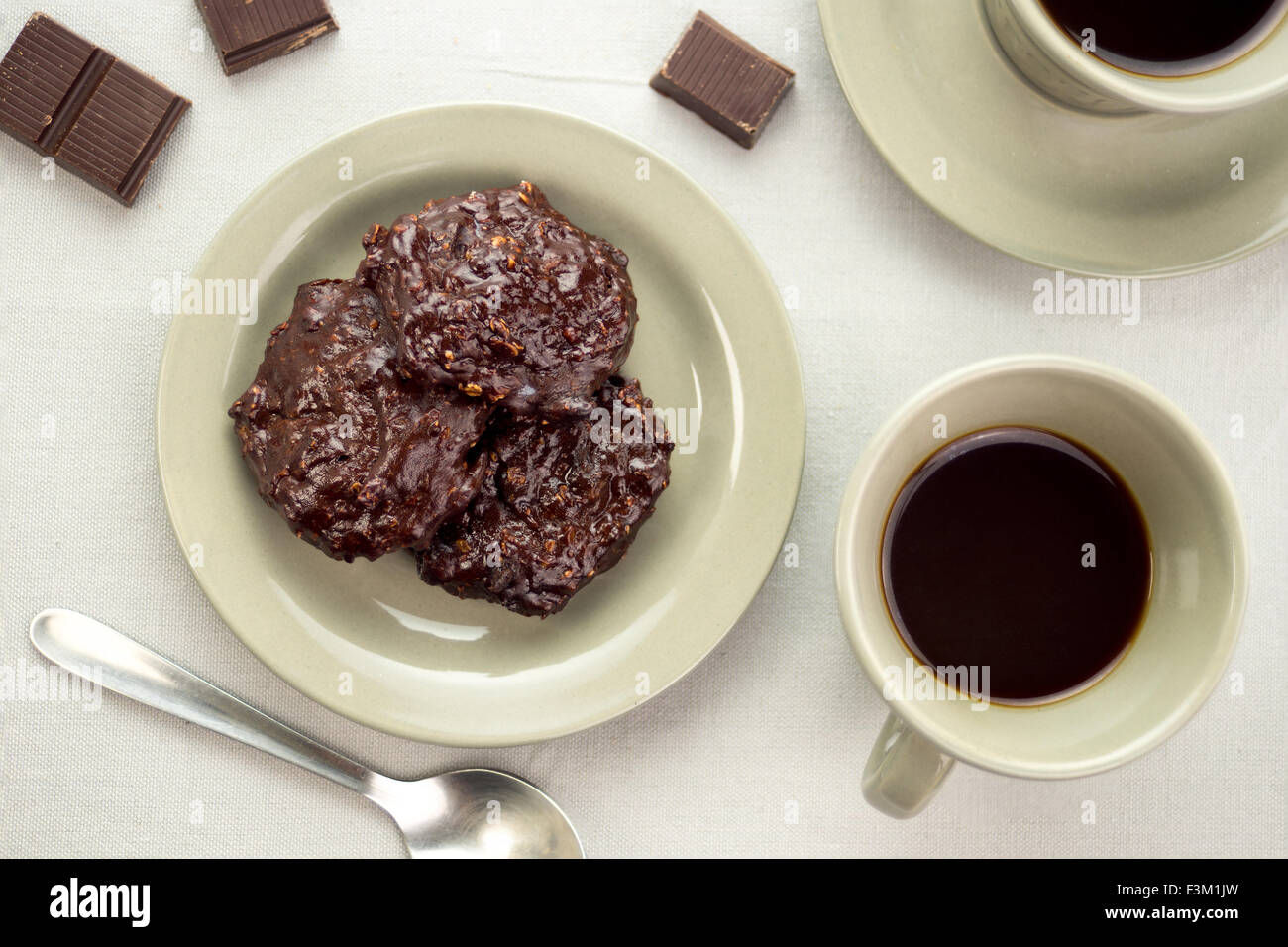 Ricca di biscotti al cioccolato in un piattino accanto a tazze di caffè nero e pezzetti di cioccolato Foto Stock