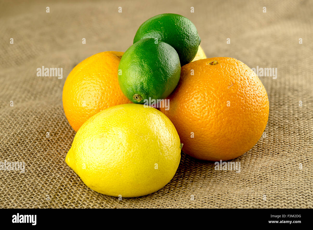 Limes, arance e limoni in pila su fattoria fresco hessian sacchetto Foto Stock