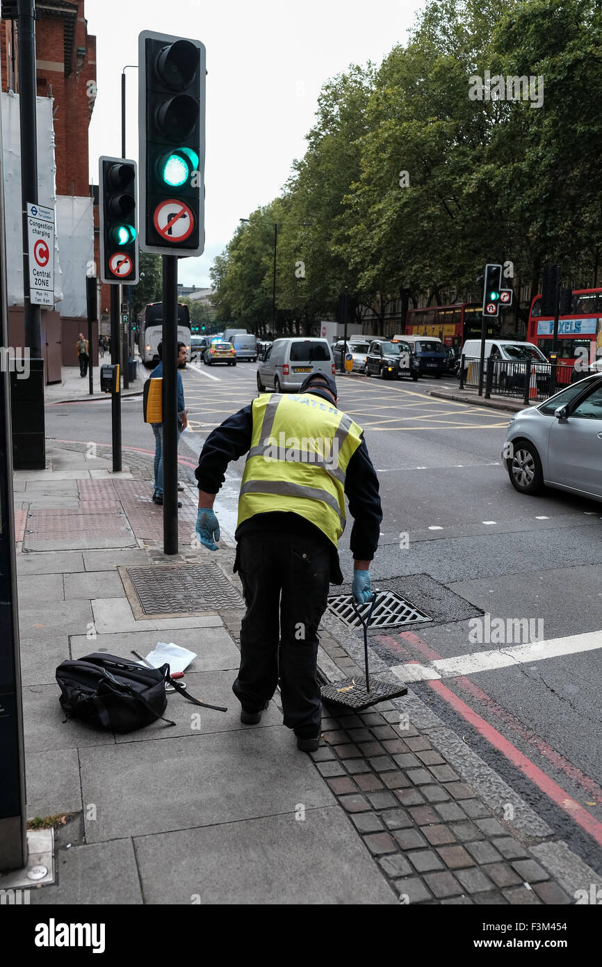 Uomo dalla società acqua tirando verso l'alto e i coperchi di scarico in London street Foto Stock