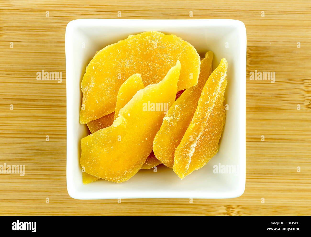 Disidratati mango essiccato in ciotola bianco su sfondo di legno Foto Stock