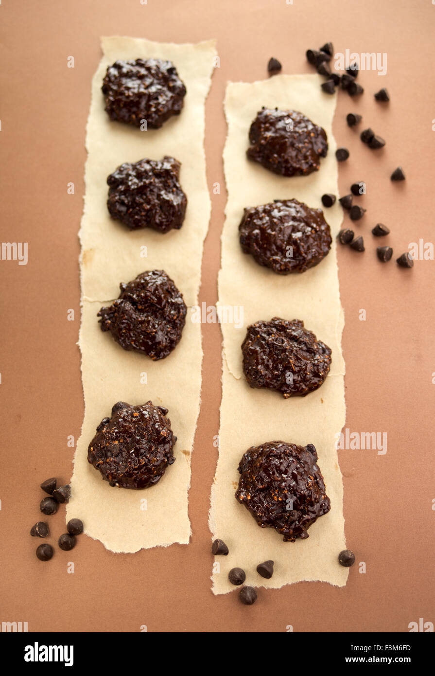 In casa dark chocolate cookies disposti artisticamente su carta pergamena, circondato da scaglie di cioccolato. Profondità di campo Foto Stock