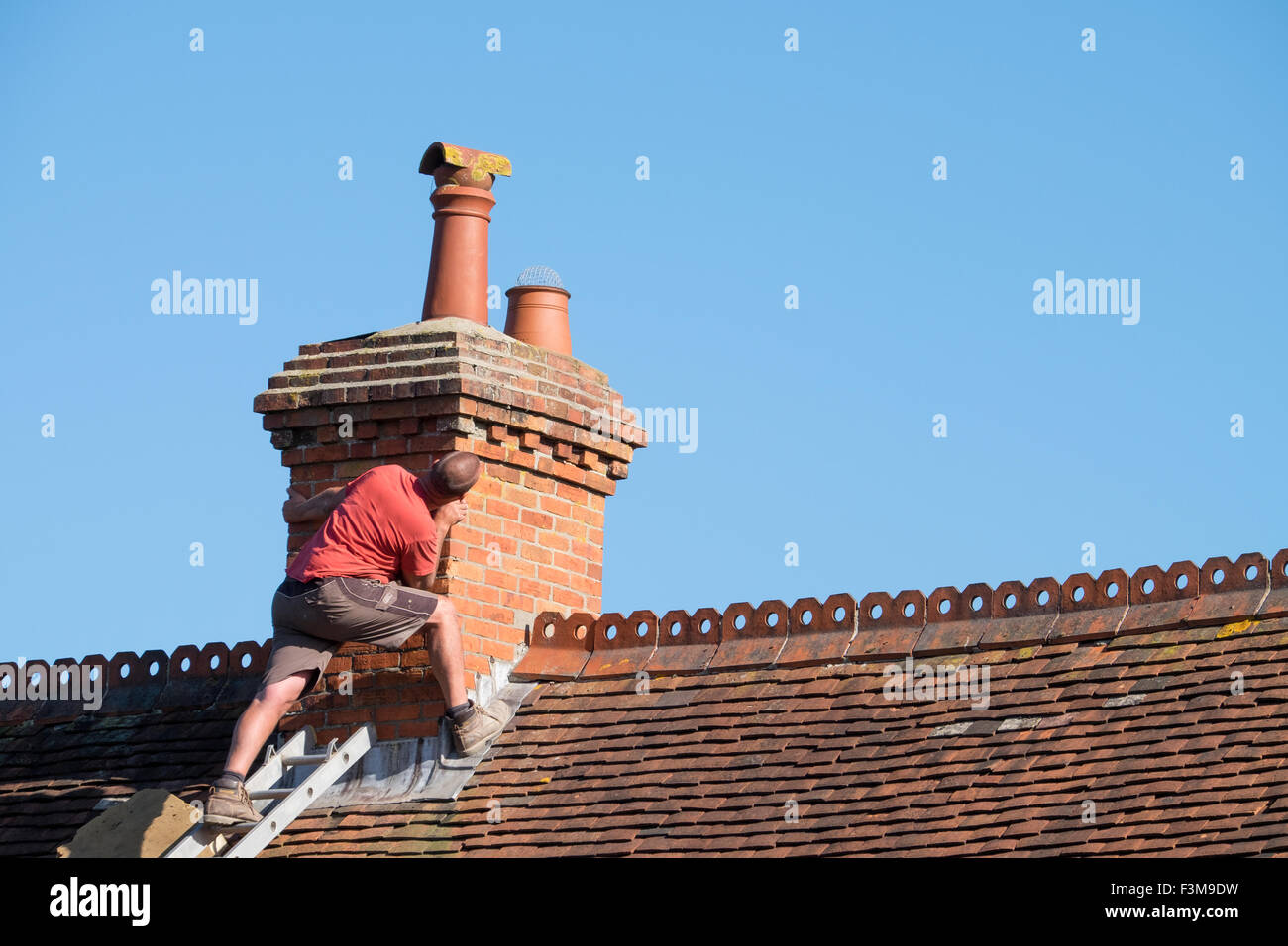 Un uomo su un tetto di ispezionare un camino per la riparazione Foto Stock