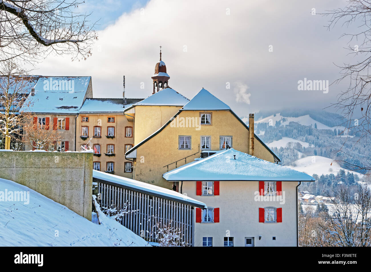 Vista della coperta di neve edifici medievali della città di Gruyeres con le alpi svizzere in background Foto Stock