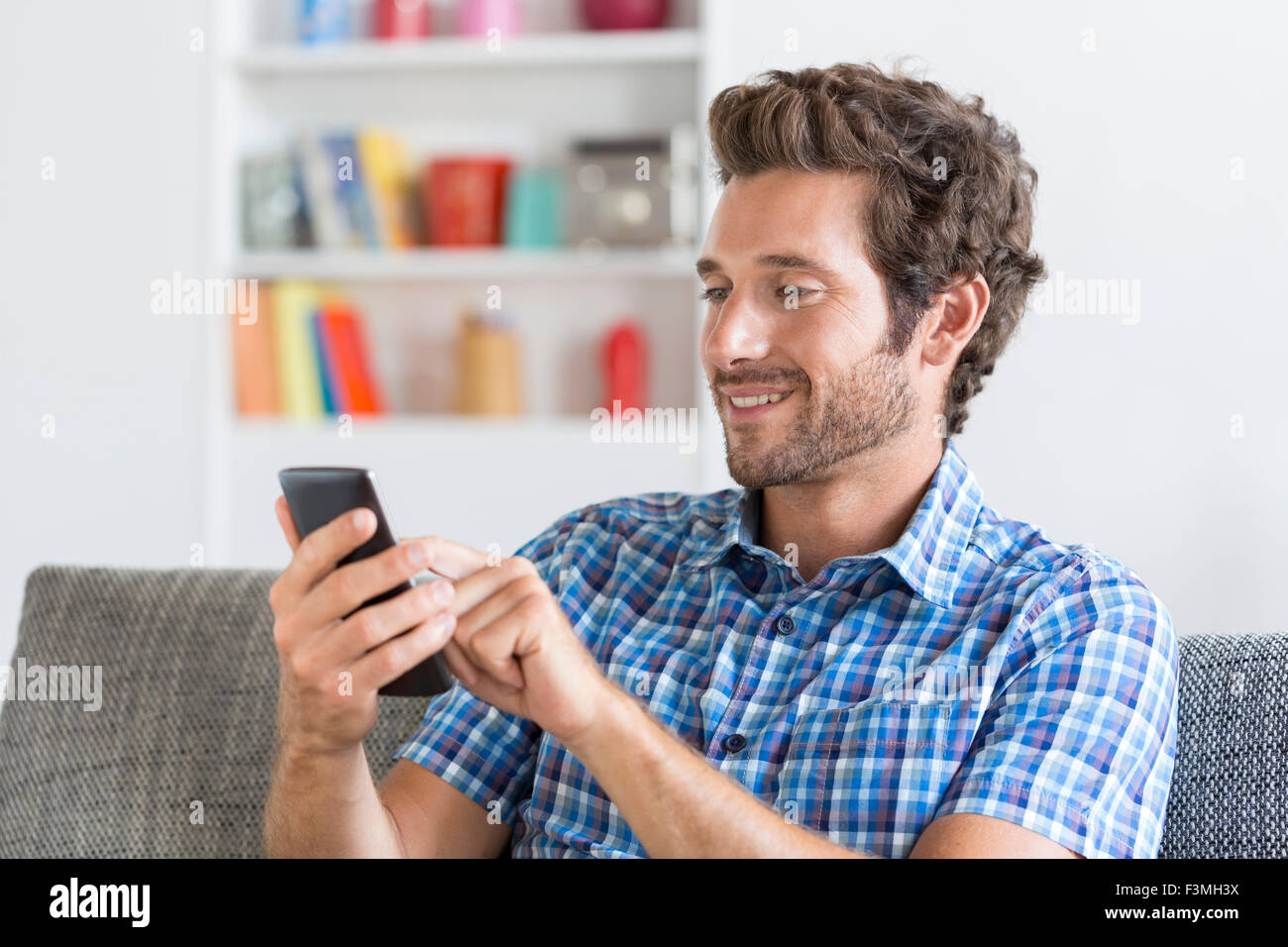 In bianco e moderno appartamento a metà uomo adulto texting messaggio sul telefono cellulare. Foto Stock