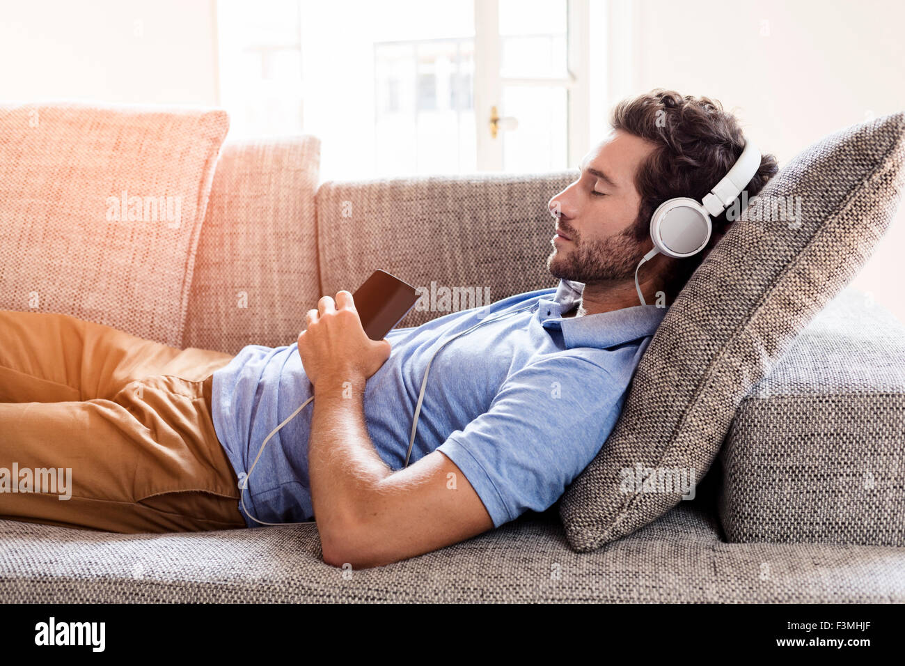 Uomo a casa sul divano ascoltando la musica con lo smartphone. Relax Foto Stock
