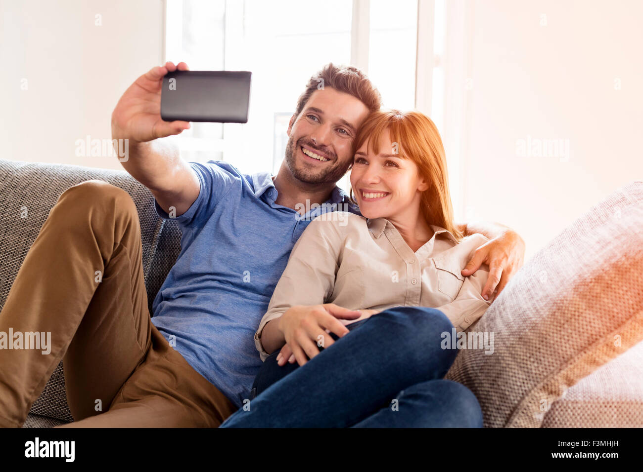 Coppia felice in amore prendendo un autoritratto con un telefono cellulare. Home divano. Lens Flare Foto Stock