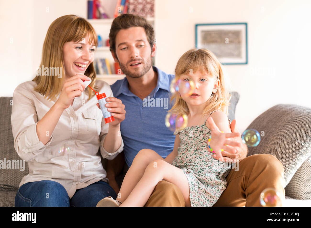 Allegro i genitori e la figlia a soffiare bolle sul divano di casa Foto Stock