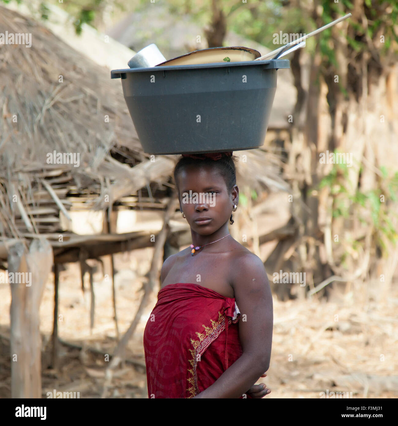 Donna africana equilibra una benna con utensili sul suo capo sul suo modo home dal fiume. Foto Stock