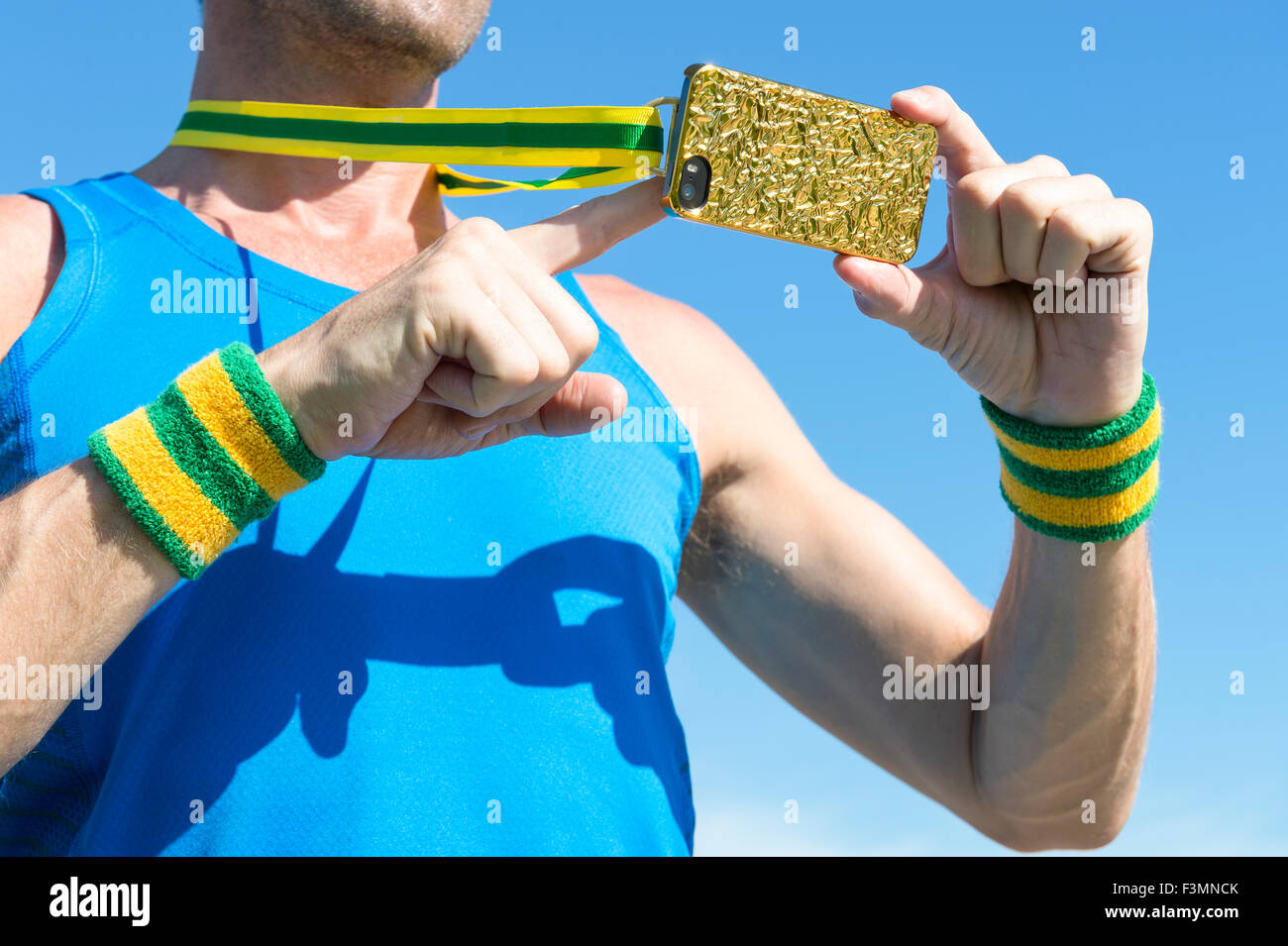 Atleta brasiliano con il verde ed il giallo polsini con medaglia d oro telefono mobile contro il cielo blu Foto Stock