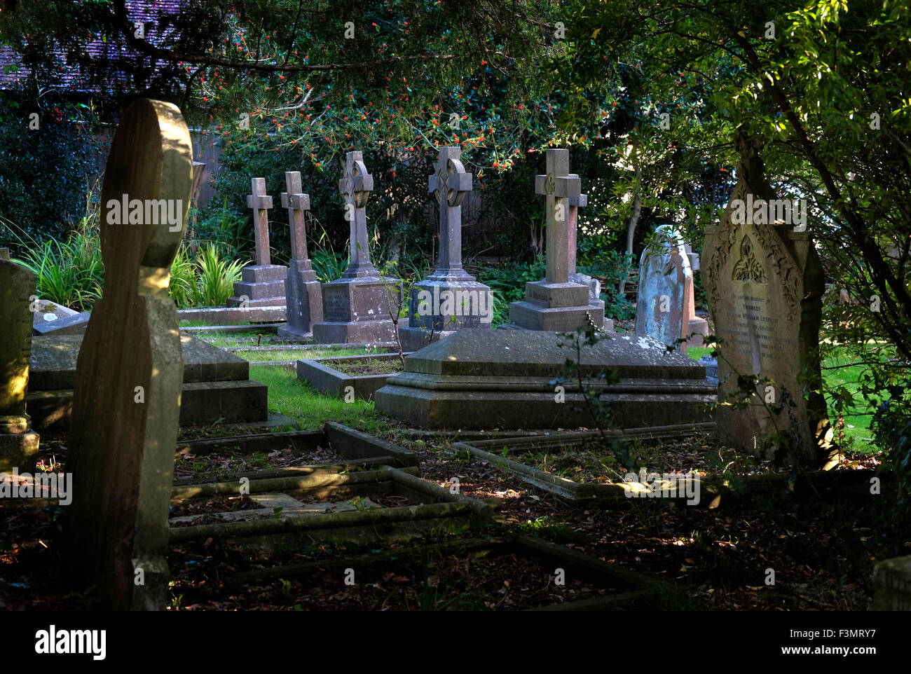 Tombe nel cimitero di una chiesa in stile vittoriano in Sneyd Park, Bristol circondato da alberi di tasso, un REGNO UNITO Foto Stock