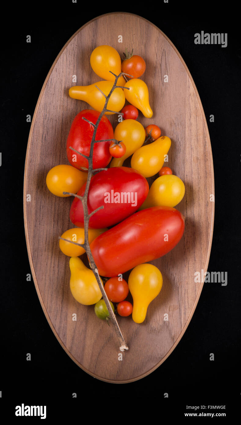 Orto biologico di rosso e di giallo pomodori ciliegia su una ciotola di legno isolato su nero Foto Stock