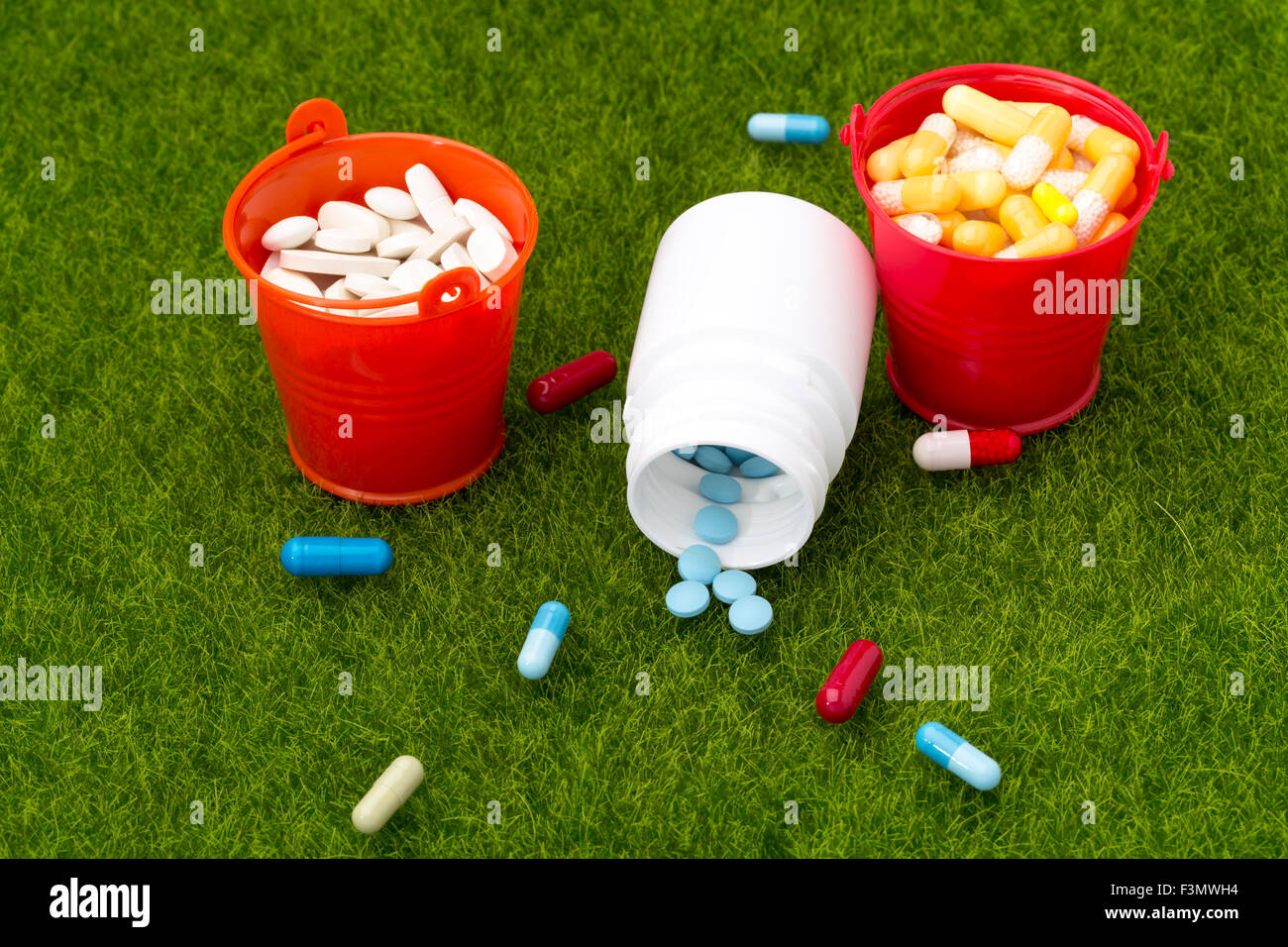 Pillole, bottiglia di pillole e due secchi pieni di pillole sull'erba verde Foto Stock