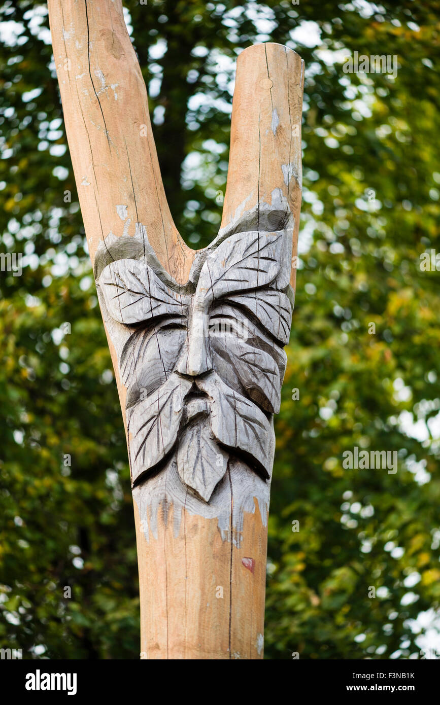 Frondose il volto dell'uomo intagliato in un palo di legno in un parco giochi per bambini. Wolverton Mill, Milton Keynes, Regno Unito. Foto Stock