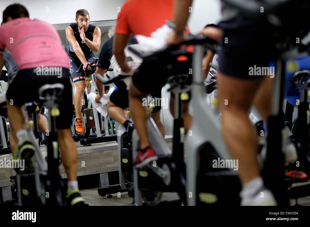 Istruttore di Fitness di fronte a persone di equitazione bicicletta stazionaria durante una lezione di spinning presso la palestra Foto Stock