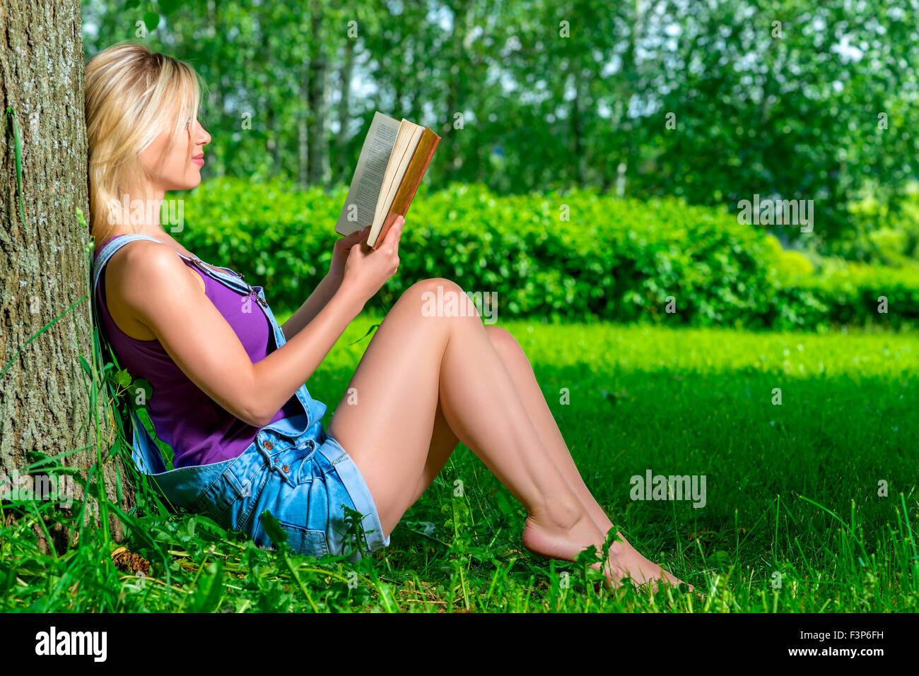 Slim giovane ragazza la lettura di un libro seduti vicino a un albero Foto Stock