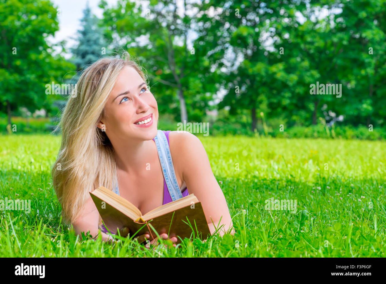 Felice ragazza sognante leggendo un libro nel parco Foto Stock
