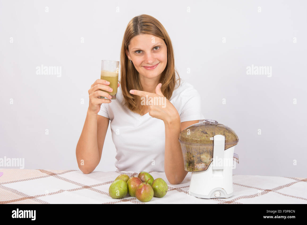 Giovane bella ragazza nella centrifuga spremute succhi di pera e sedersi a  un tavolo con un bicchiere di succo di frutta in mano Foto stock - Alamy