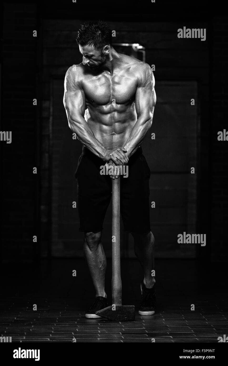 Ritratto di una adatta fisicamente l uomo che mostra il suo ben addestrato corpo e tenendo un martello Foto Stock